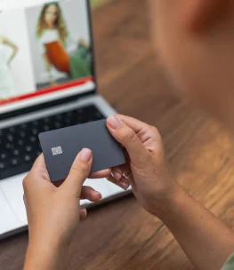 Delicate hands hold a credit card against a laptop screen displaying an online fashion clothing store's website, exemplifying seamless online shopping.